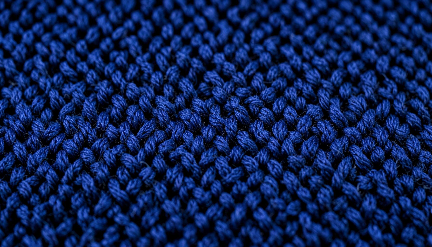 A close-up of a tightly knitted fabric in deep navy blue, showing the intricate loop structure and rich texture of premium knitwear